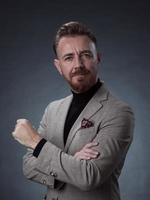 portrait d'un homme d'affaires senior élégant et élégant avec une barbe et des vêtements d'affaires décontractés en studio photo isolé sur fond sombre gesticulant avec les mains