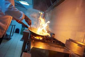 le chef de la cuisine de l'hôtel prépare la nourriture avec le feu photo