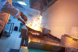 le chef de la cuisine de l'hôtel prépare la nourriture avec le feu photo