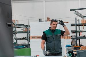 intérieur de l'usine d'ingénierie de l'industrie lourde avec un ouvrier industriel utilisant une meuleuse d'angle et coupant un tube métallique. entrepreneur en uniformes de sécurité et casques de sécurité fabriquant des structures métalliques. photo