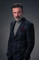 portrait d'un homme d'affaires senior élégant et élégant avec une barbe et des vêtements d'affaires décontractés en studio photo isolé sur fond sombre gesticulant avec les mains