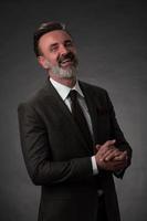 portrait d'un homme d'affaires senior élégant et élégant avec une barbe et des vêtements d'affaires décontractés en studio photo isolé sur fond sombre gesticulant avec les mains