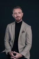 portrait d'un homme d'affaires adulte portant un costume à la mode et assis dans un studio moderne sur une chaise élégante sur fond noir photo