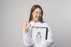 jeune femme ophtalmologiste avec des lunettes tenant un tableau des yeux sur fond bleu studio, concept de soins de santé photo