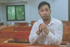 un jeune homme asiatique fidèle mains en geste de prière assis seul sur une chaise prie et espère bonne chance, succès, pardon. pouvoir de la religion, croyance, foi de dieu, idées de concept de culte. photo