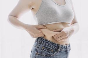 belle grosse femme avec ruban à mesurer, elle utilise sa main pour presser l'excès de graisse isolé sur fond blanc. elle veut perdre du poids, le concept de chirurgie et décomposer les graisses sous le photo