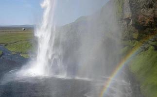 un arc-en-ciel devant la cascade de seljalandsfoss sur la côte sud de l'islande lors d'une journée ensoleillée photo