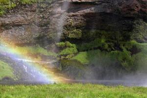 un arc-en-ciel devant la cascade de seljalandsfoss sur la côte sud de l'islande lors d'une journée ensoleillée photo