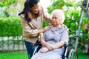 le soignant aide une femme âgée asiatique handicapée patiente assise sur un fauteuil roulant dans le parc, concept médical. photo