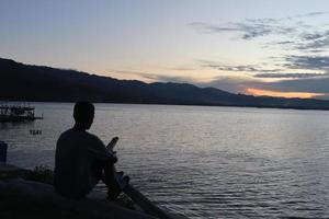 silhouette d'un jeune homme debout au bord du lac en profitant du coucher de soleil. atmosphère paisible dans la nature photo