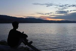silhouette d'un jeune homme debout au bord du lac en profitant du coucher de soleil. atmosphère paisible dans la nature photo
