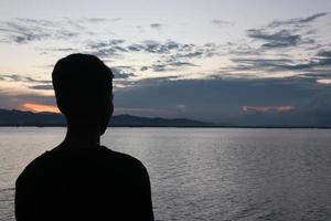 silhouette d'un jeune homme debout au bord du lac en profitant du coucher de soleil. atmosphère paisible dans la nature photo