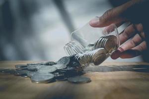 main d'homme mettant un verre de pièces de monnaie d'économie sur une table en bois photo