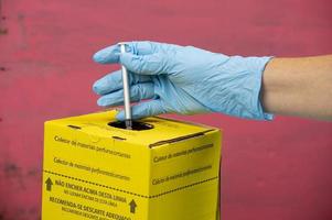 boîte de collecte des déchets hospitaliers contaminés avec la main plaçant une seringue photo