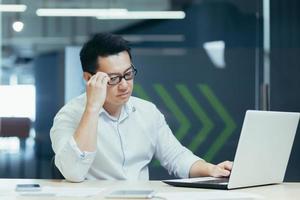 portrait jeune homme d'affaires asiatique sérieux et concentré dans des verres, travaillant avec un ordinateur portable au bureau