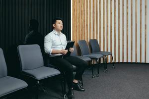 un homme asiatique attend dans la salle de réception un entretien pour un emploi dans un bureau, une banque, une entreprise photo
