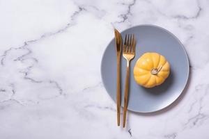 citrouille orange sur une assiette bleue avec des couverts. concept minimaliste du menu d'automne photo
