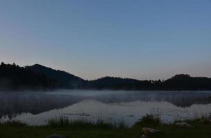 lac avec brouillard s'élevant de la surface de l'eau au lever du soleil photo