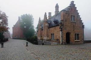 matin brumeux solitaire sur l'ancien parc de la ville médiévale de bruges, belgique. maisons en briques anciennes, pont et chaussée vue grand angle photo