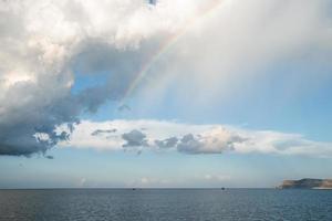 vue panoramique sur le magnifique arc-en-ciel jetant un coup d'œil à travers les nuages sur le paysage marin photo