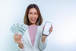 femme heureuse asiatique souriante tenant un téléphone mobile intelligent en ligne et de l'argent en dollars à portée de main. photo