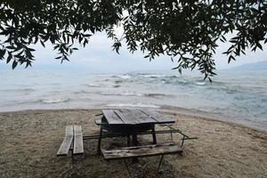 table et bancs sur le sable au bord du lac sous un arbre photo
