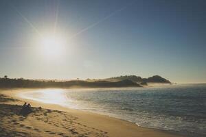 deux copains s'assoient sur le rivage de la plage au milieu des empreintes de pas au coucher du soleil. image originale du domaine public de wikimedia commons photo