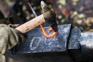 le forgeron forge la boucle de fer avec un marteau sur l'enclume photo