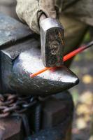 Le forgeron forge une tige d'acier chauffée au rouge sur l'enclume photo