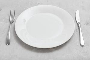 assiette blanche avec couteau, cuillère sur béton gris photo