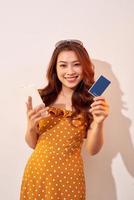 portrait d'une fille heureuse tenant un téléphone portable et une carte de crédit isolée sur fond beige photo