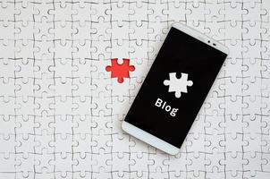 un grand smartphone moderne avec écran tactile se trouve sur un puzzle blanc dans un état assemblé avec inscription. Blog photo