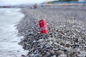 antalya, turquie - 18 mai 2021 la boîte de conserve rouge coca cola originale se trouve sur de petits cailloux ronds près du bord de mer. coca-cola sur la plage turque photo