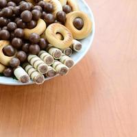 des tubules croustillants, des boules fondantes au chocolat et des bagels se trouvent dans une assiette blanche sur une table en bois. mélange de diverses douceurs photo