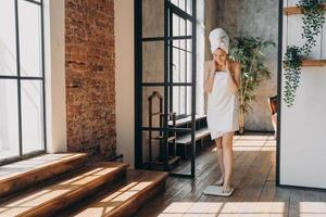 fille enveloppée dans une serviette mesurant le poids à l'aide d'une balance au sol électronique après la douche. minceur, bien-être photo