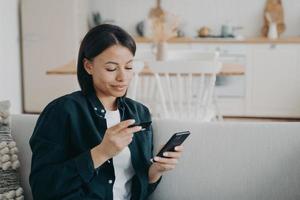 femme souriante tenant une carte de crédit bancaire, un smartphone, utilisant un service bancaire en ligne à la maison. banque en ligne photo