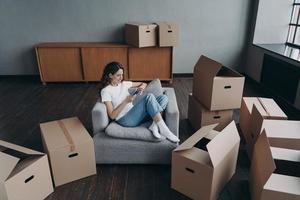 une femme utilisant un téléphone, achète des meubles, choisit un service de relocalisation pour déplacer des objets emballés dans une nouvelle maison photo