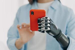 application mobile pour personnes handicapées. fille avec bras prothétique bionique tenant un smartphone dans les mains photo