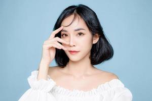 femme asiatique cheveux courts avec une peau fraîche parfaite et propre. modèle féminin mignon avec maquillage naturel et yeux pétillants sur fond bleu isolé. soin du visage, cosmétologie, concept de beauté. photo