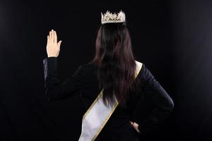 portrait de la moitié du corps du concours de beauté miss pageant en costume intelligent asiatique blazer chemise robe avec ceinture de couronne de diamants argentés, mode maquillage sourire vague main, studio éclairage fond noir isolé photo