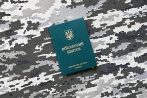 sumy, ukraine - 20 mars 2022 carte d'identité militaire ukrainienne sur tissu avec texture de camouflage pixélisé. tissu avec motif camouflage en formes de pixels gris, marron et vert avec jeton personnel de l'armée ukrainienne photo