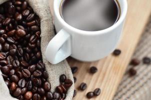 un sac plein de grains de café bruns et une tasse blanche de café chaud se trouvent sur une surface en bois photo