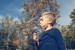 enfant soufflant pissenlit dans le parc. photo