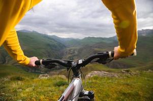 un gros plan du cycliste de la main de la jeune fille sur le guidon d'un vélo de montagne sur fond de rochers et de montagnes épiques. vélo de montagne. cycliste filles photo