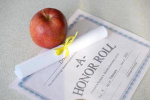 un tableau d'honneur se trouve sur une table avec un petit rouleau et une pomme rouge. documents d'éducation photo