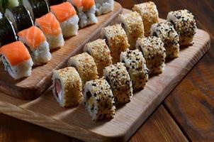 un ensemble de sushis composé d'un certain nombre de rouleaux est situé sur une planche à découper en bois sur une table dans la cuisine d'un bar à sushis. un plat traditionnel de la cuisine orientale photo