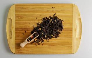thé noir aux agrumes secs, banane et pétales de fleurs. spatule en bois avec du thé et une poignée de mélange de thé sur une planche de bois photo