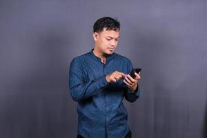 heureux homme asiatique tapant des sms sur fond gris. isolé, concept d'entreprise photo