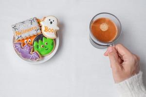 main de femme tenant une tasse de café en mangeant des biscuits d'halloween drôles. bonne fête d'halloween, astuce ou menace, bonjour octobre, automne automne, concept traditionnel, fête et vacances photo