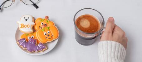 main de femme tenant une tasse de café en mangeant des biscuits d'halloween drôles. bonne fête d'halloween, astuce ou menace, bonjour octobre, automne automne, concept traditionnel, fête et vacances photo